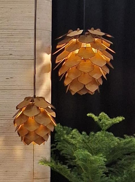 Two Käpy pendant lamps glowing warmly against a dark background with pine branches below