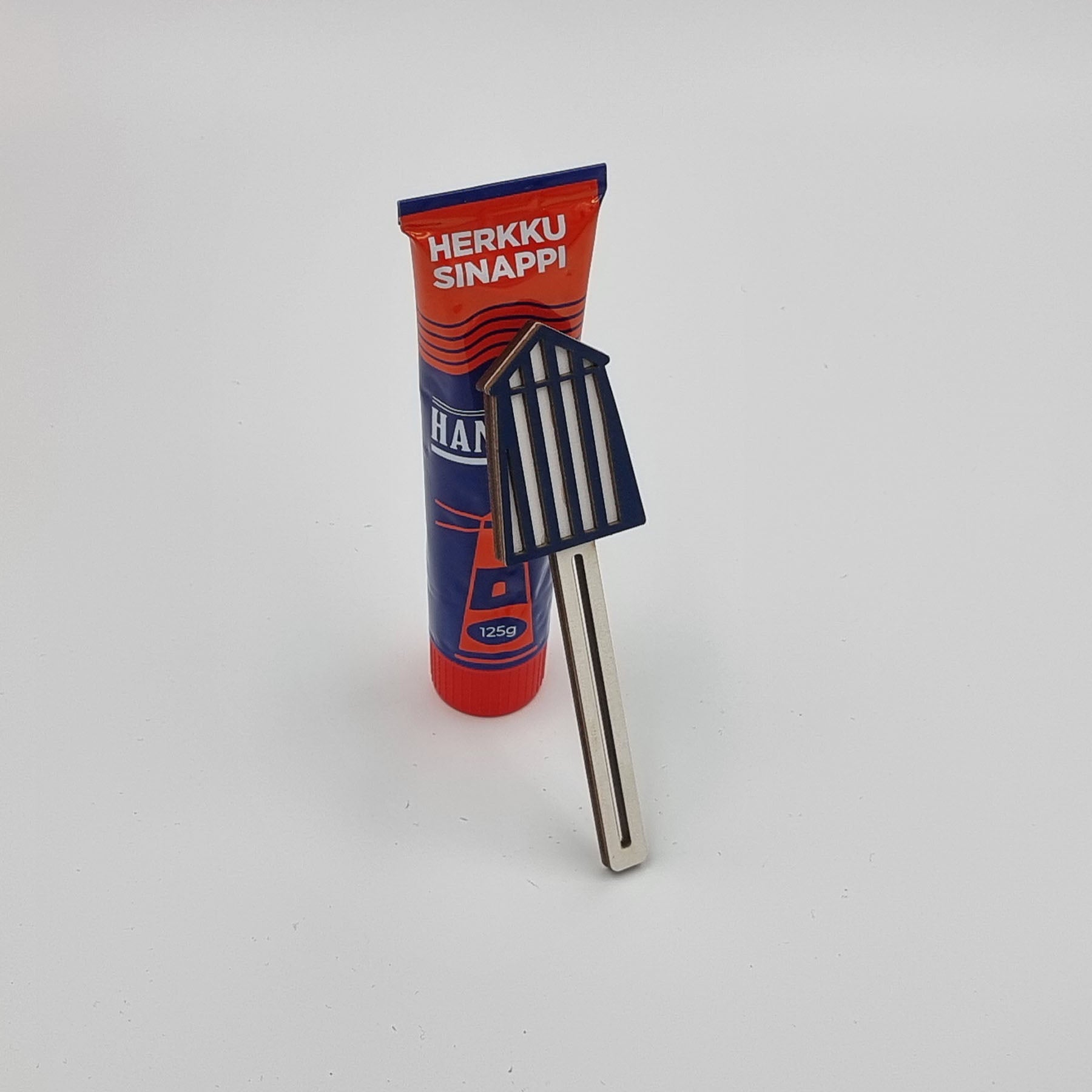A tube squeezer tool with a blue and red colored mustard tube placed beside it on a white surface.