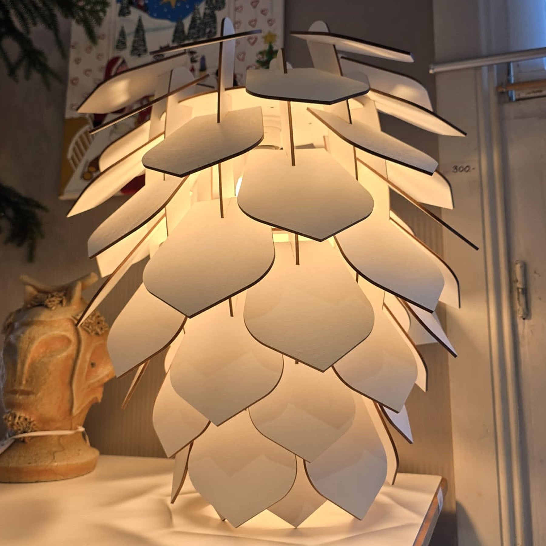 A ceiling-mounted lamp with a geometric pine cone design made of birch veneer, illuminated and placed over a decorative object.