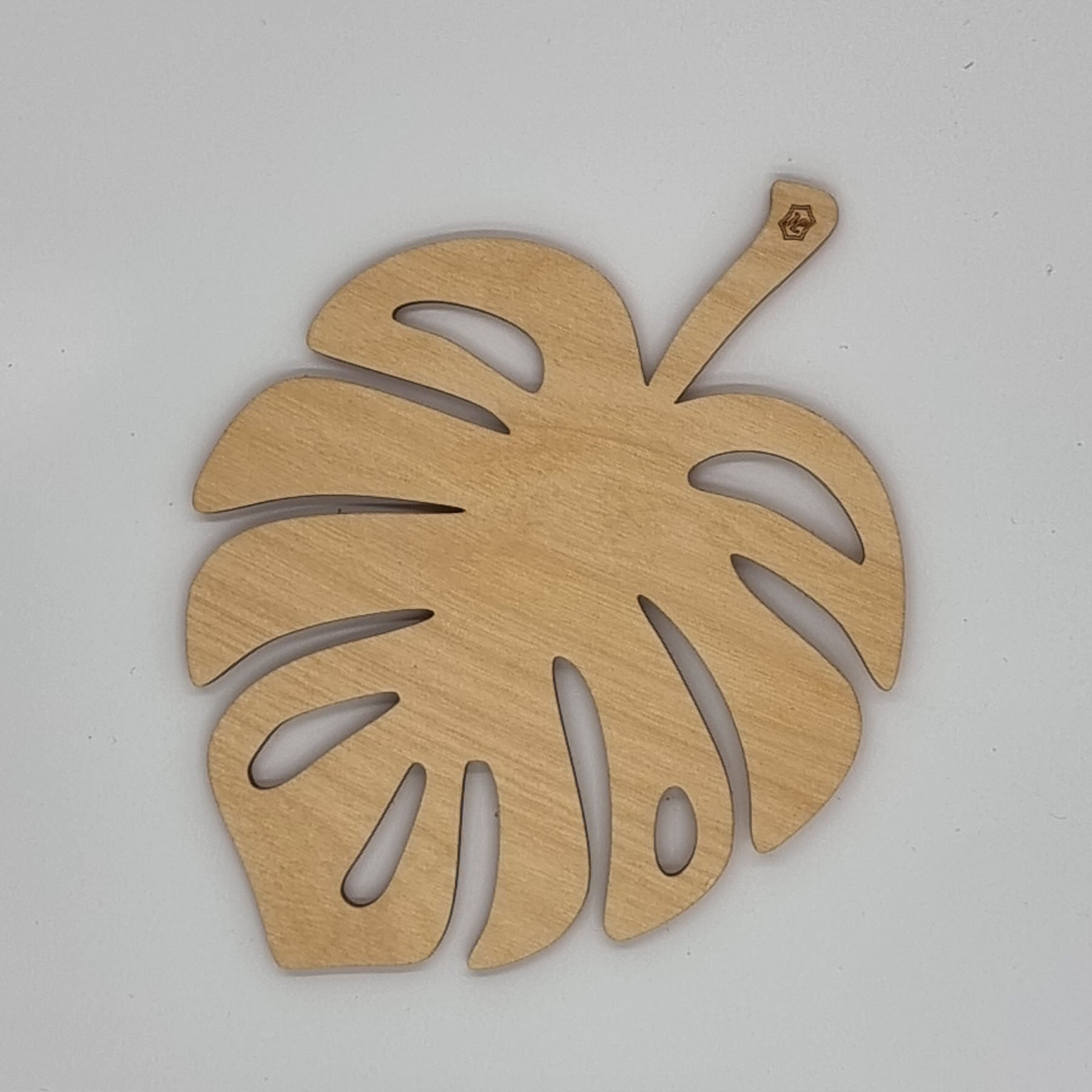 A wooden trivet designed in the shape of a Monstera leaf with a visible hanging hole on the top right corner.