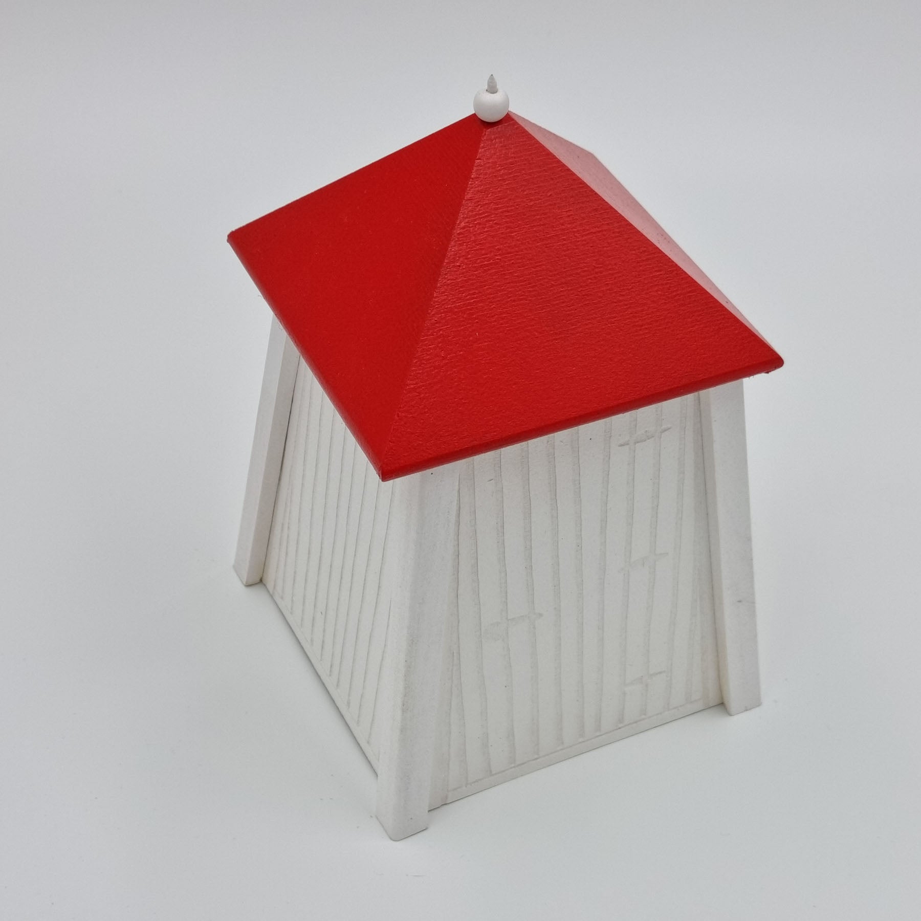 A handcrafted wooden miniature of a traditional beach cabin from Hanko, Finland, featuring a red roof and white painted walls