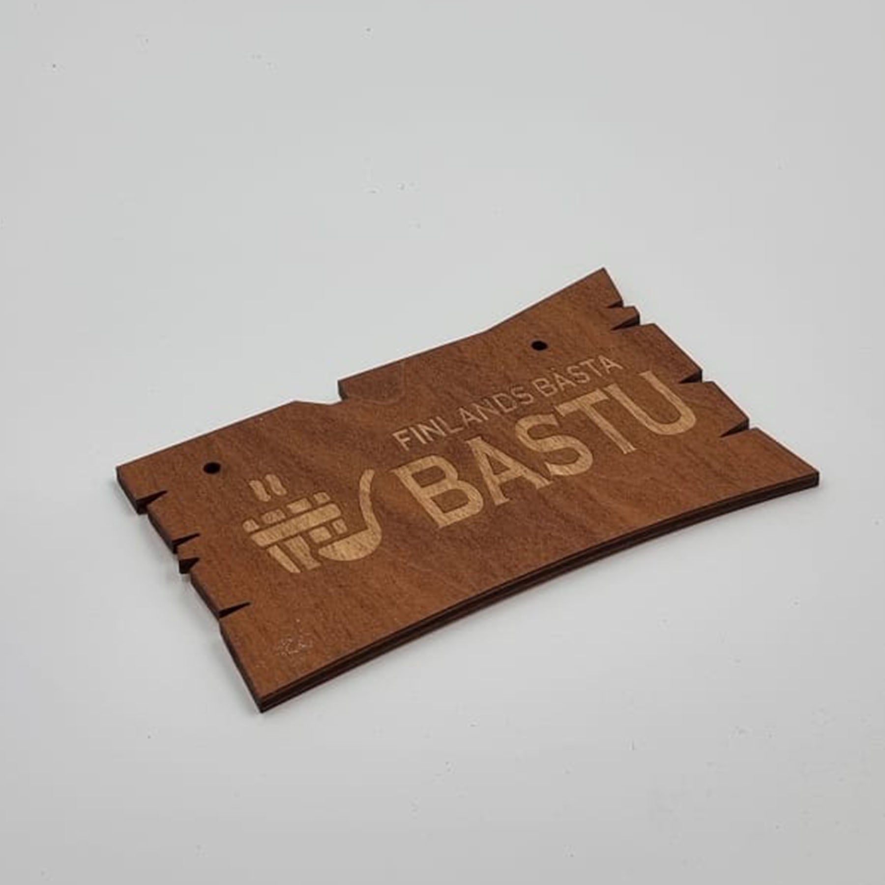 A wooden sauna sign with laser-engraved text 'BASTU' and what appears to be a sauna logo, in a curved rectangular shape, with pre-drilled holes for hanging.