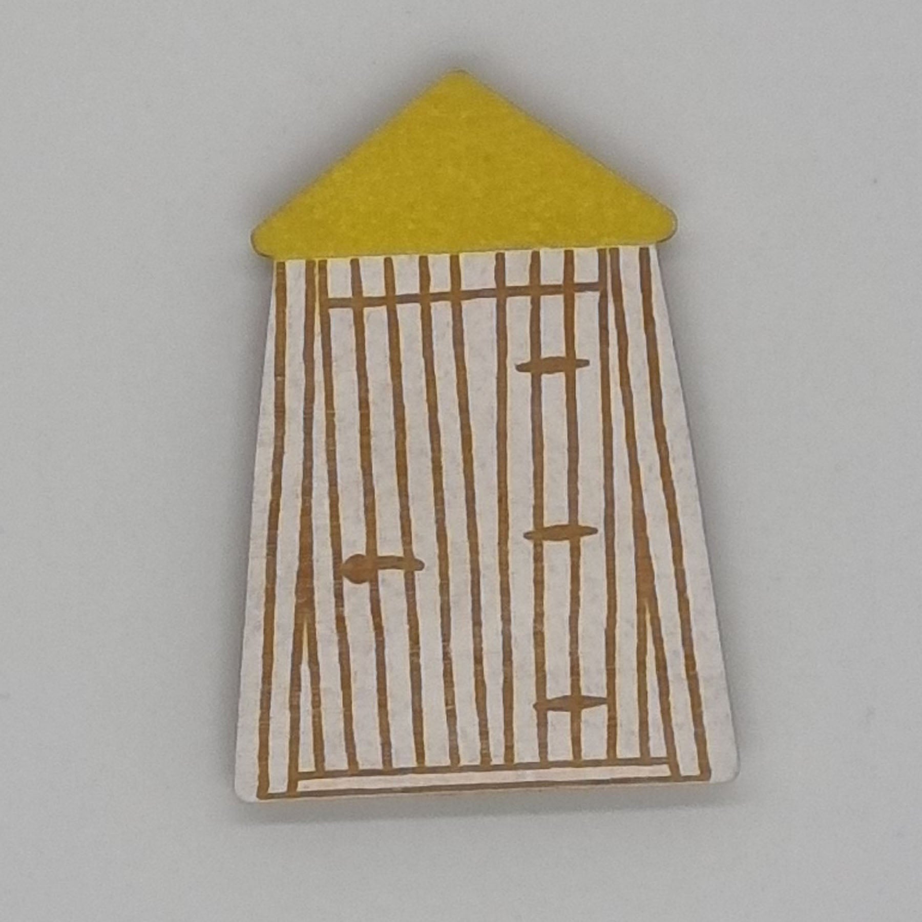 A handcrafted bathing room magnet with a yellow conical roof and a striped pattern resembling a shack or hut.