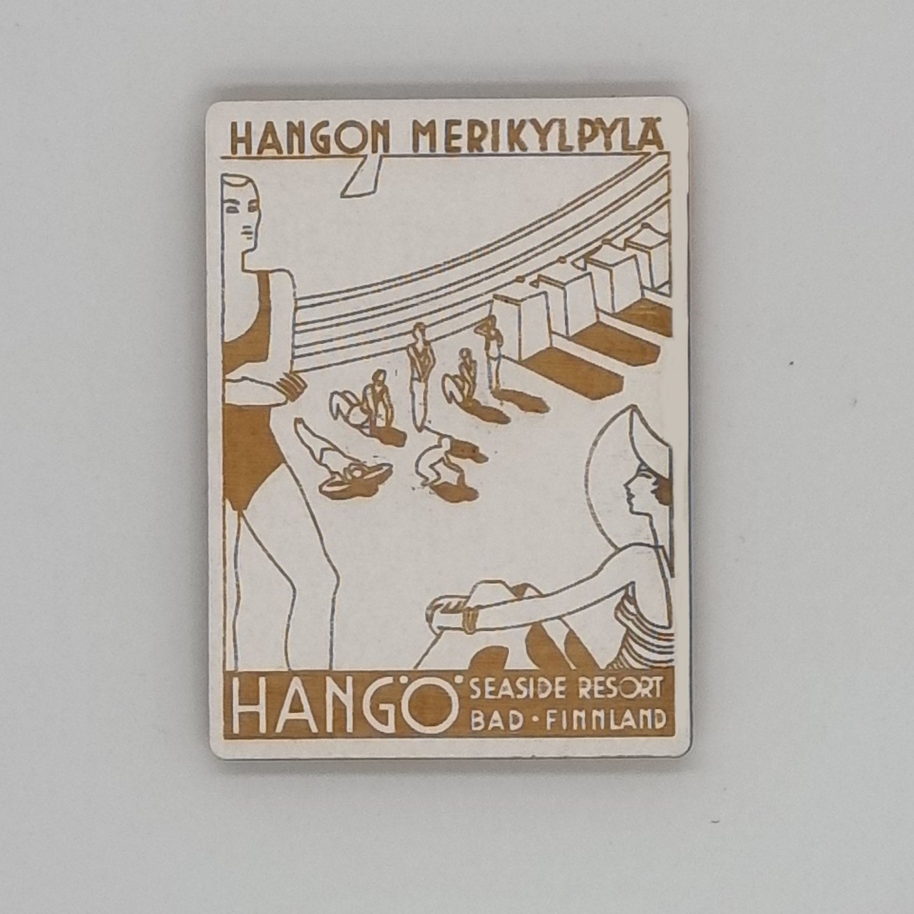 A rectangular magnet with a illustration of people at a beach, including a merry-go-round, sun loungers, and a seaside resort sign.